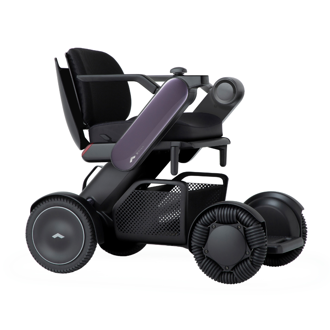The Whill Model C2 Smart Power Chair is a compact, portable mobility device with a sleek black frame, large wheels, armrests, mesh storage basket, and is FDA-compliant as a Class II medical device designed for comfort and modern convenience.